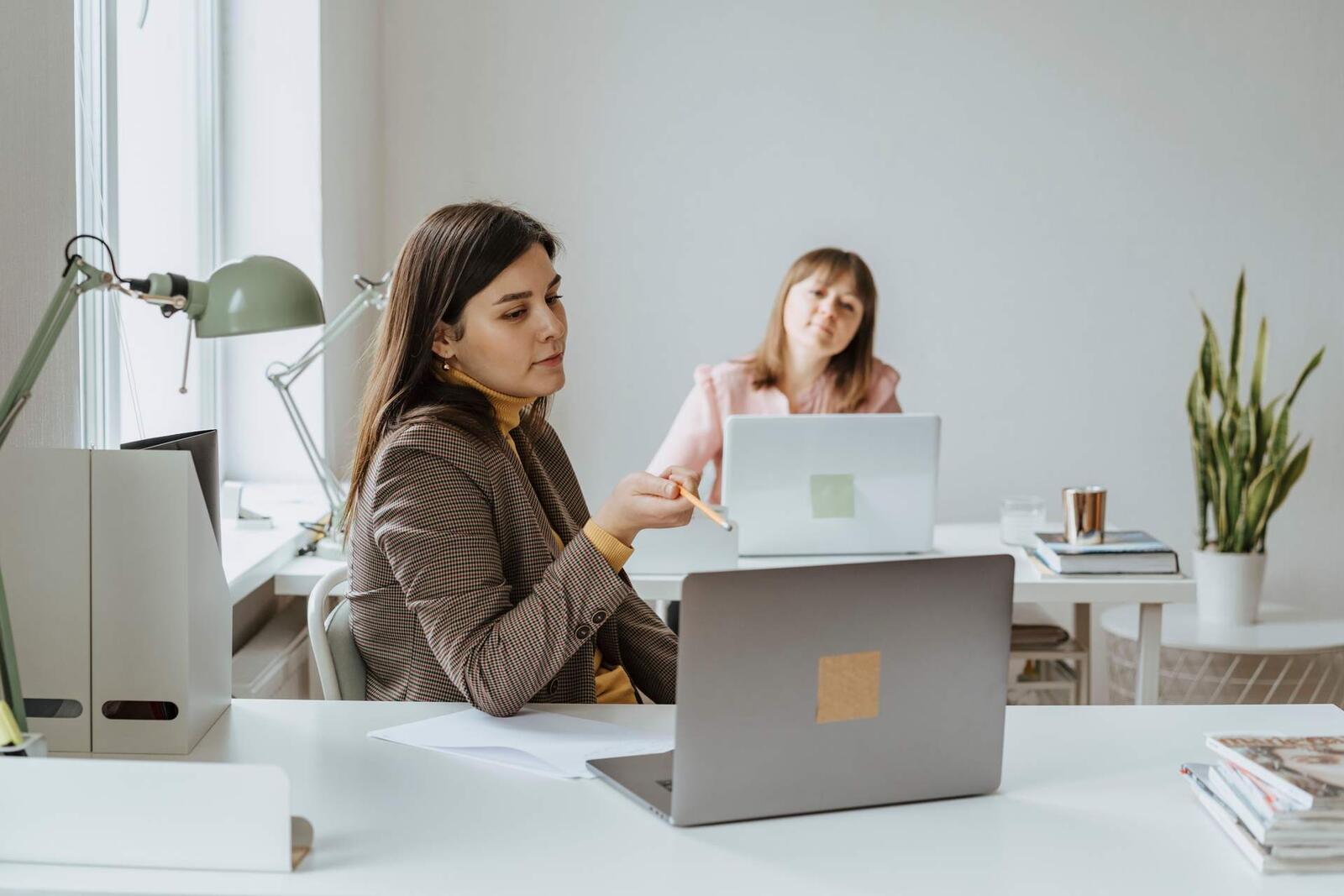 Advisor in a houndstooth blazer reviewing documents with a colleague at a white office desk