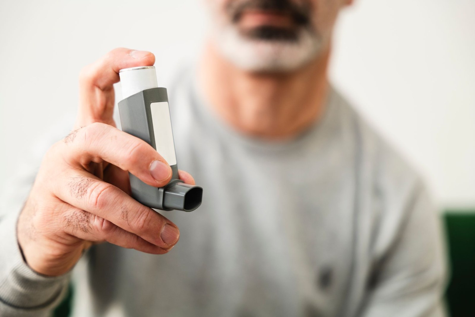 Man holding a metered-dose inhaler toward the camera, face softly out of focus