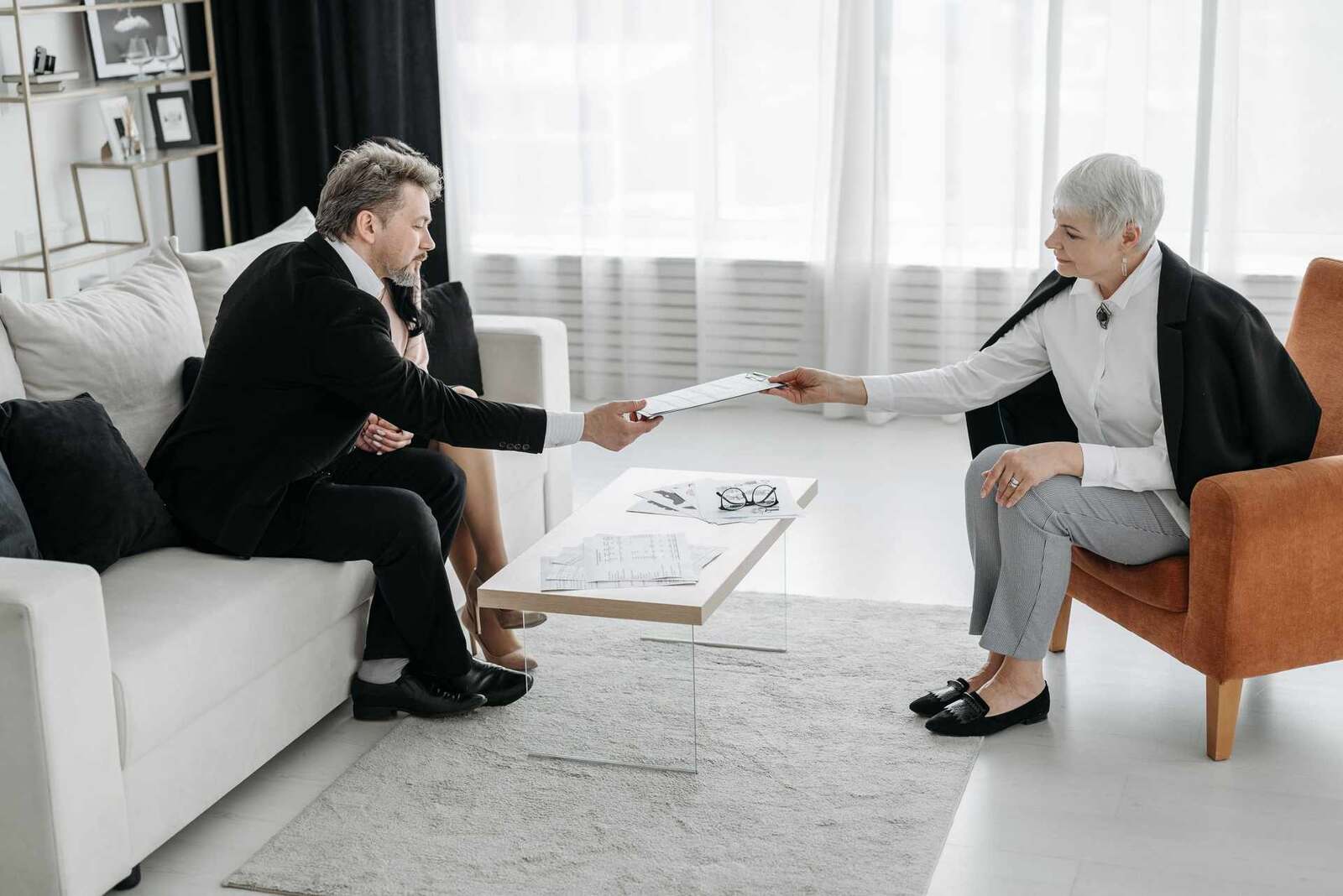 Two colleagues in a bright lounge, one handing a document across a low table to the other