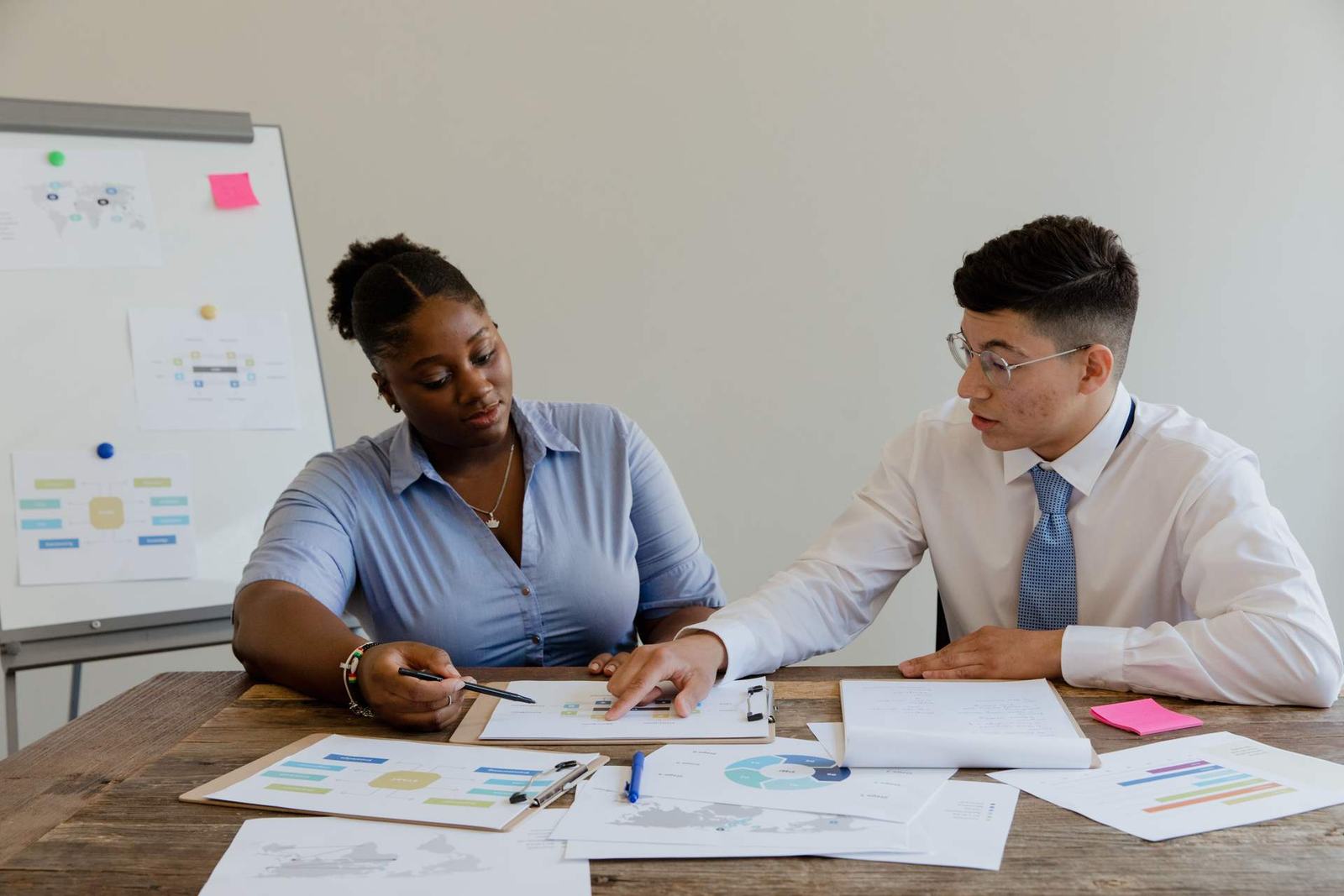 Two regulatory colleagues reviewing process-flow diagrams and data charts spread across a conference table