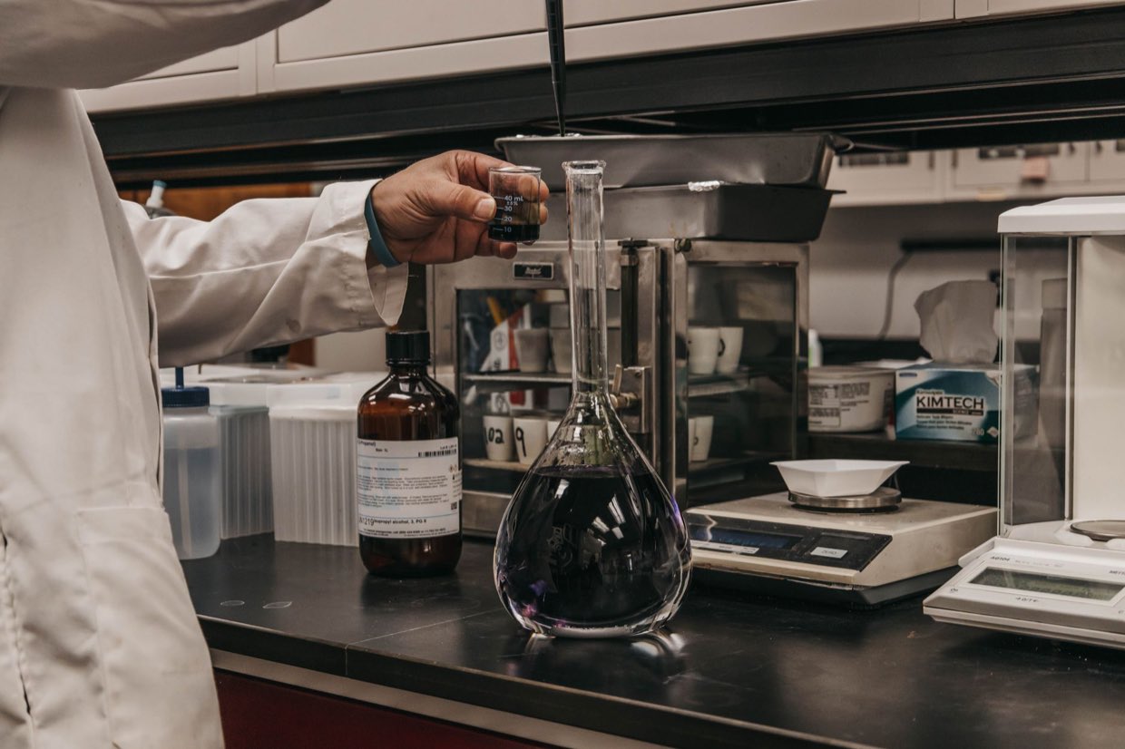 A scientist measuring solution into a volumetric flask at a laboratory bench