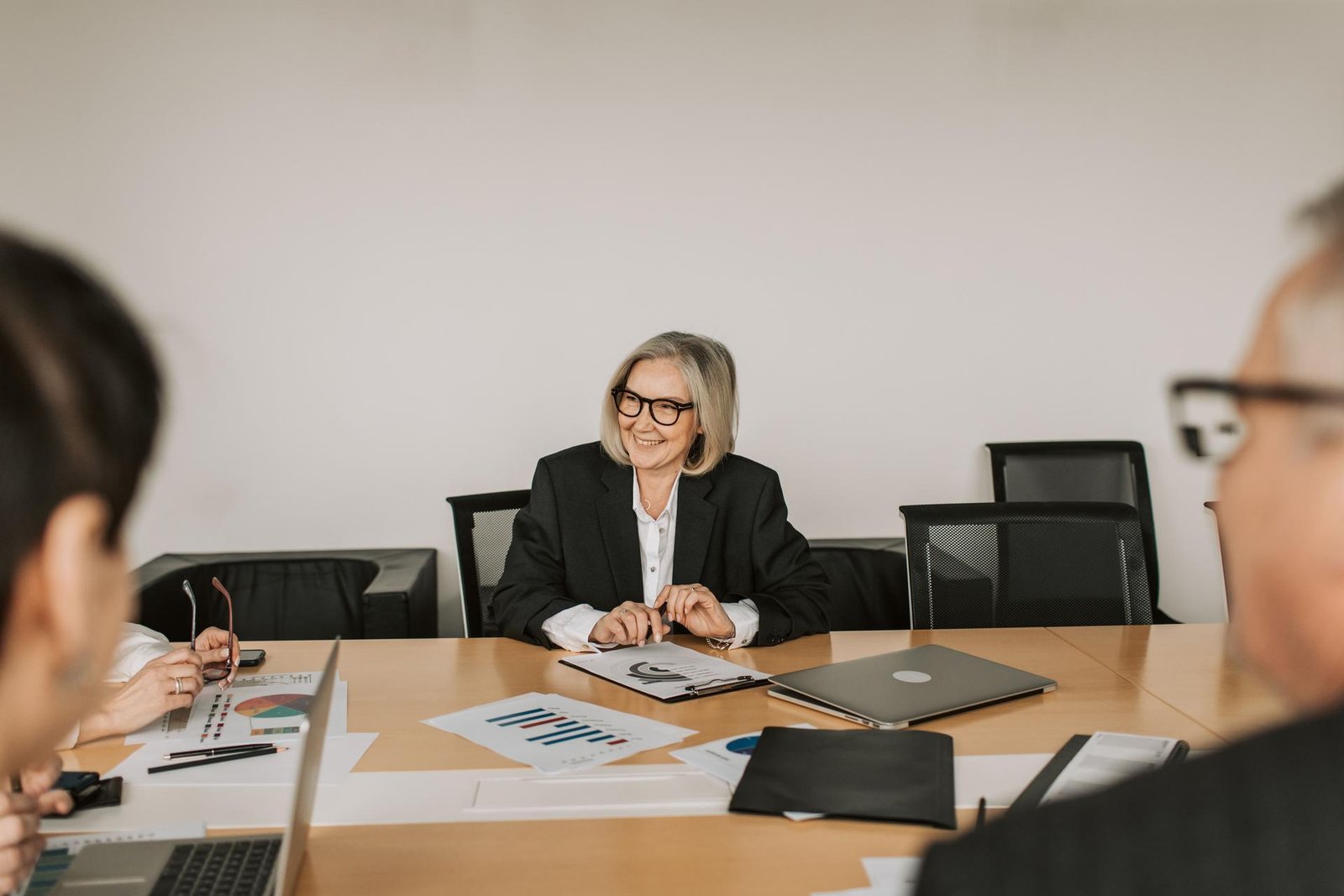 A smiling woman reviews printed charts and data pages with colleagues at a conference table