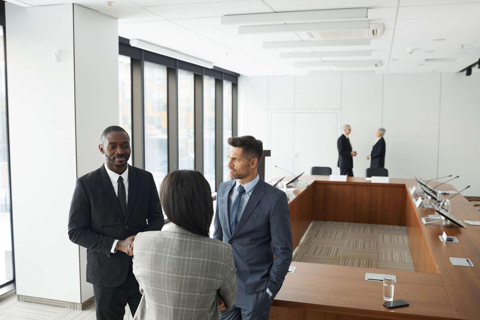 Colleagues in a bright glass-walled boardroom discussing documents before a meeting
