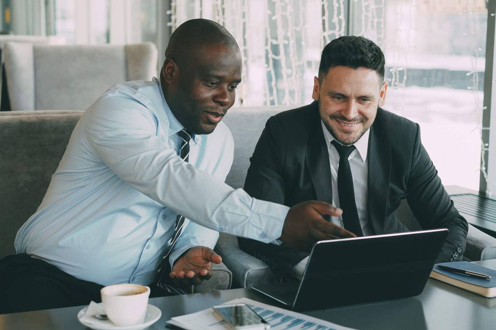 Two colleagues smiling and reviewing data together on a laptop in a bright lounge setting