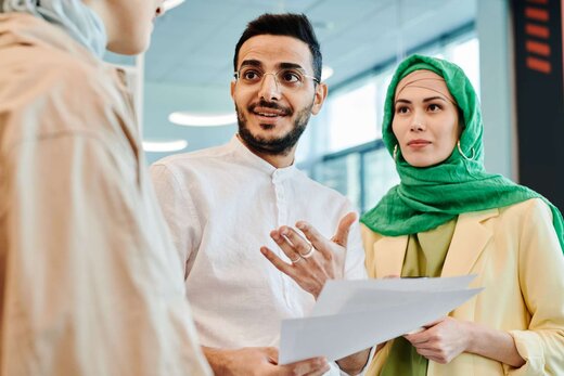Three colleagues standing in a bright office discussing a printed document together