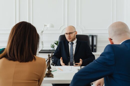Regulatory advisor in a navy suit explaining a document across a white desk to two colleagues in a bright office