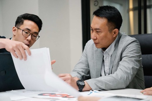 Two quality colleagues in business attire reviewing printed inspection findings together at a desk