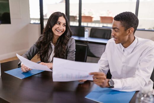 Two regulatory colleagues smiling while reviewing a printed chart document at a boardroom table