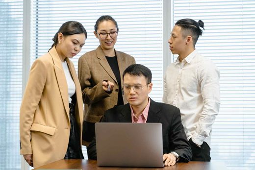Four colleagues gathered around a laptop reviewing analysis on screen in a bright conference room