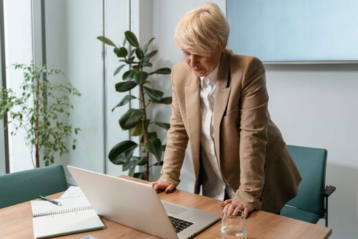 Senior regulatory advisor in a beige blazer reviewing a document on a laptop in a bright boardroom