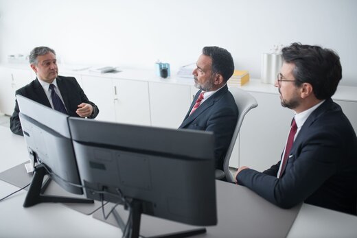 Three regulatory colleagues in dark suits discussing documents at a desk in a bright white office