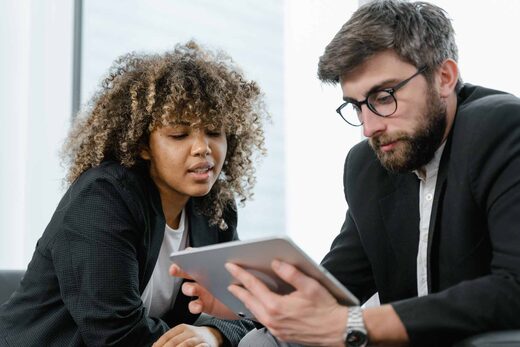 Two colleagues in blazers reviewing a tablet together by a bright office window