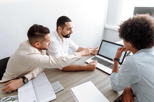 Three colleagues in business attire review a document and a laptop together in a bright office