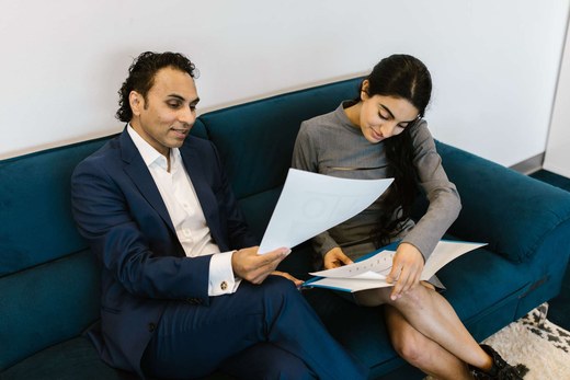 Two colleagues seated on an office sofa reviewing a printed study document together