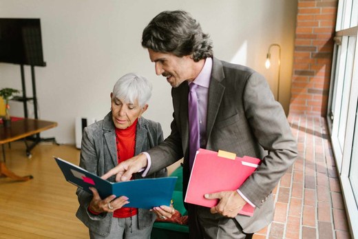 Two colleagues reviewing a folder of documentation together near a sunlit window