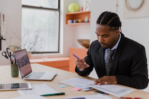 Regulatory professional in a dark suit reviewing printed compliance documents at a desk