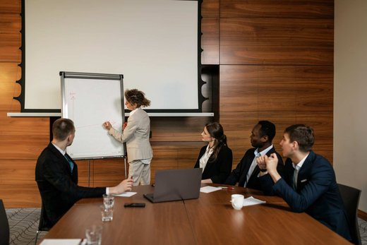 A diverse group of colleagues in business attire reviewing a hand-drawn chart on a flipchart in a wood-paneled conference room