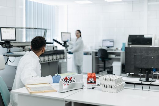 Two lab scientists in a clean, brightly lit laboratory reviewing sample vials and data at a workstation