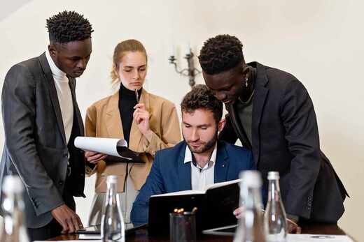 Four colleagues in a bright room reviewing a bound document together