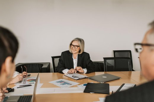A smiling woman reviews printed charts and data pages with colleagues at a conference table