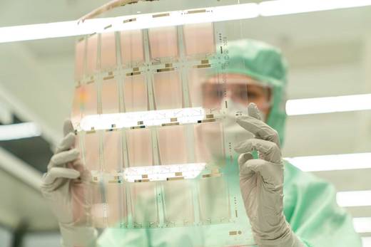 Cleanroom technician inspecting a transparent sheet of flexible printed circuits