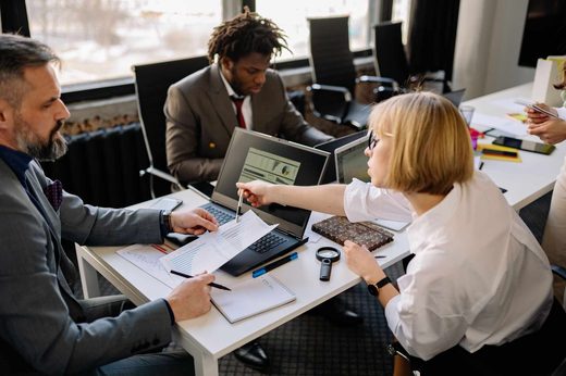 Colleagues reviewing printed data charts and a laptop showing analytics around an office table