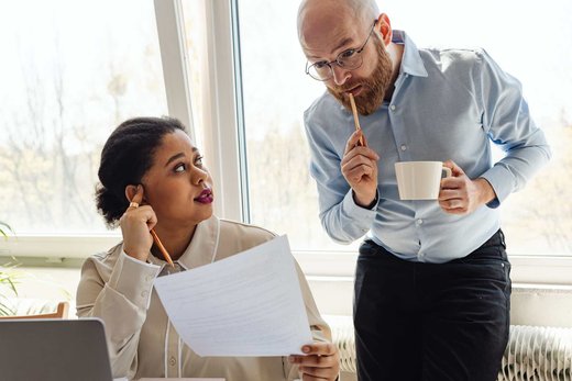 Two colleagues closely reviewing a printed document with skeptical expressions