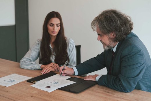 Two colleagues reviewing and signing a document with charts spread across a conference table