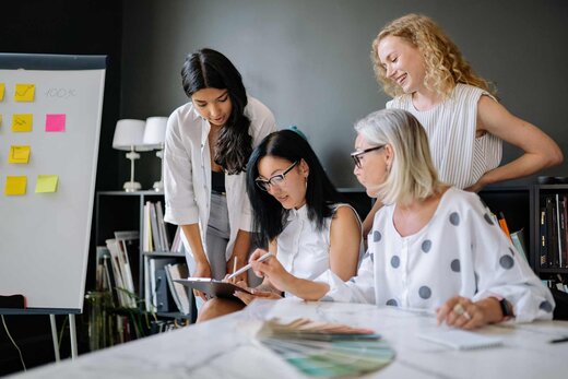 Four colleagues in a bright studio review a clipboard and a fan of color swatches together