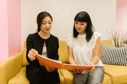Two colleagues reviewing an orange folder of documents together on a yellow sofa