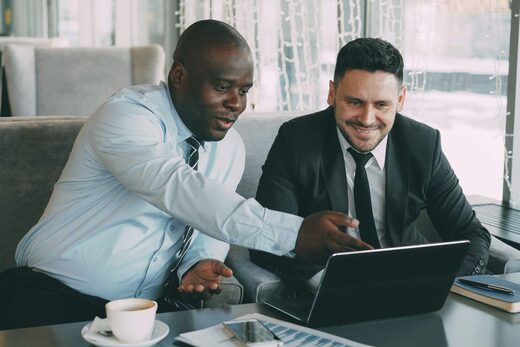 Two colleagues smiling and reviewing data together on a laptop in a bright lounge setting