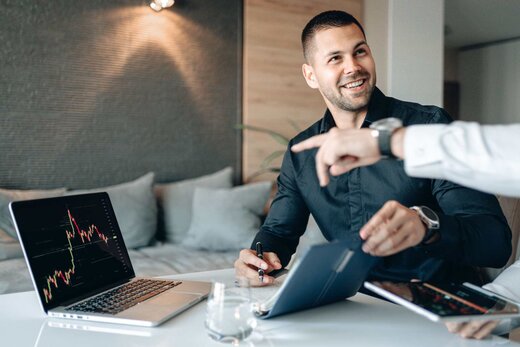 A consultant smiles while reviewing a data chart on a laptop and handing over a document in a bright meeting space