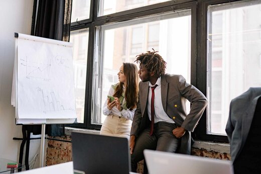 Two colleagues reviewing handwritten charts on a flipchart by a window