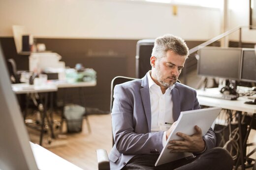 Executive in a grey blazer reviewing a notebook of handwritten notes in a bright office