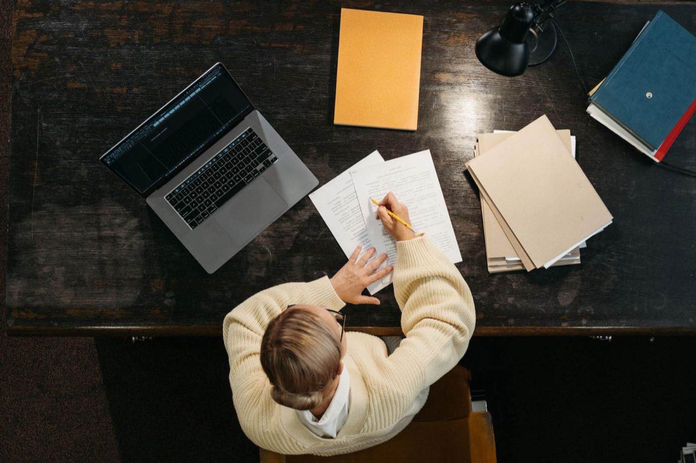 A person writing documentation at a desk with a laptop and papers