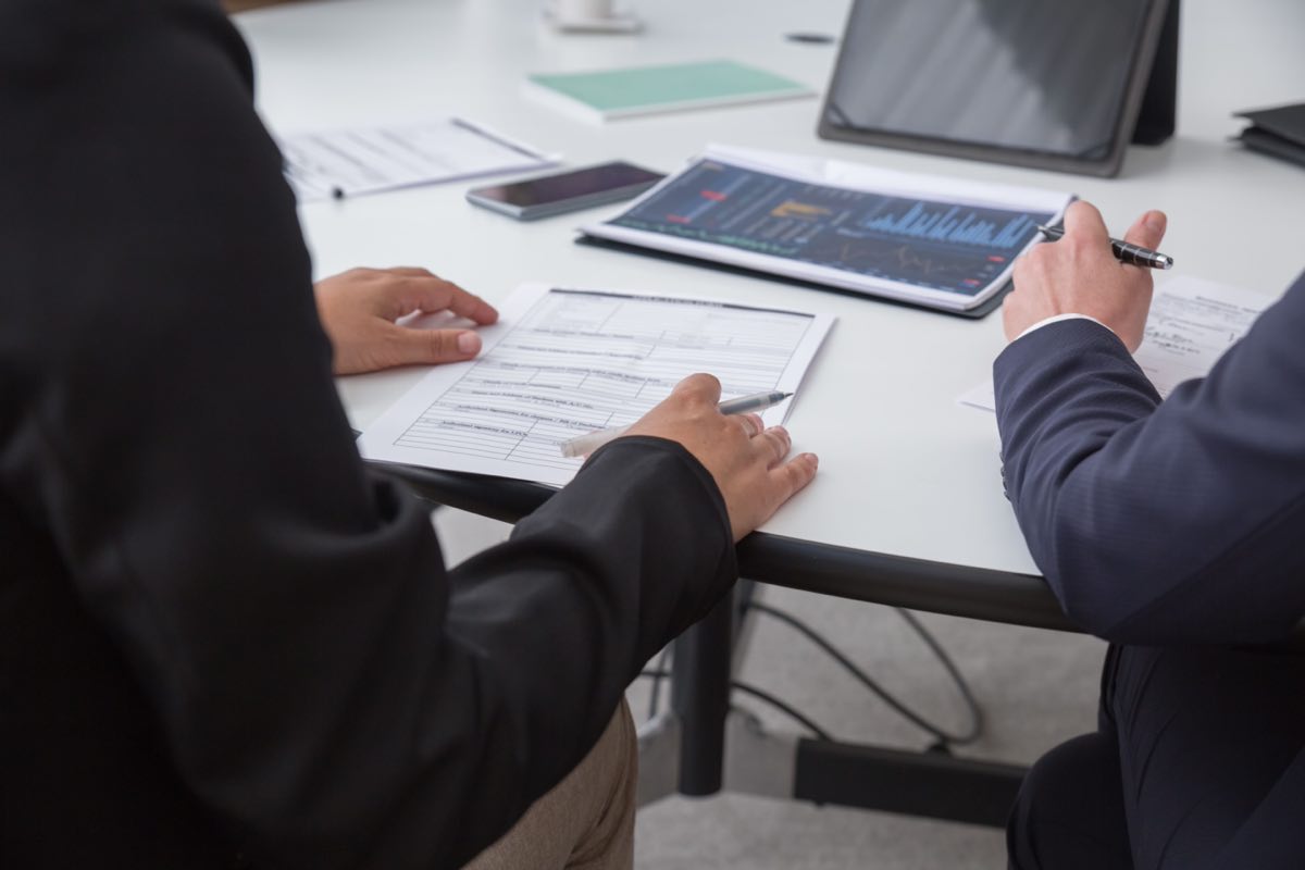 Analysts working through printed figures and a tablet dashboard at a meeting table