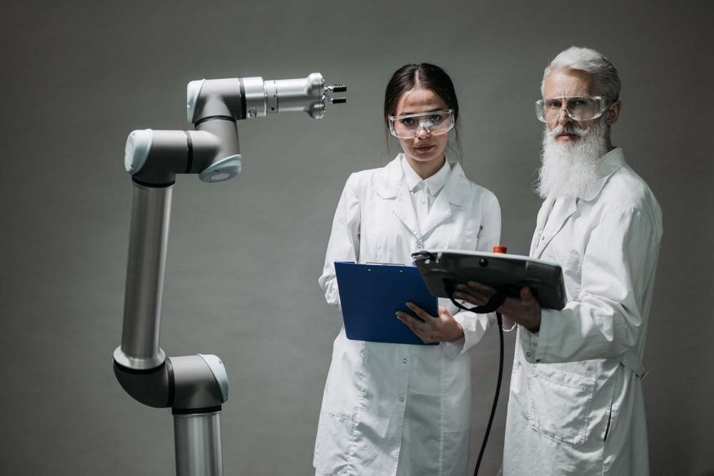 Two scientists in lab coats analyzing a robotic arm
