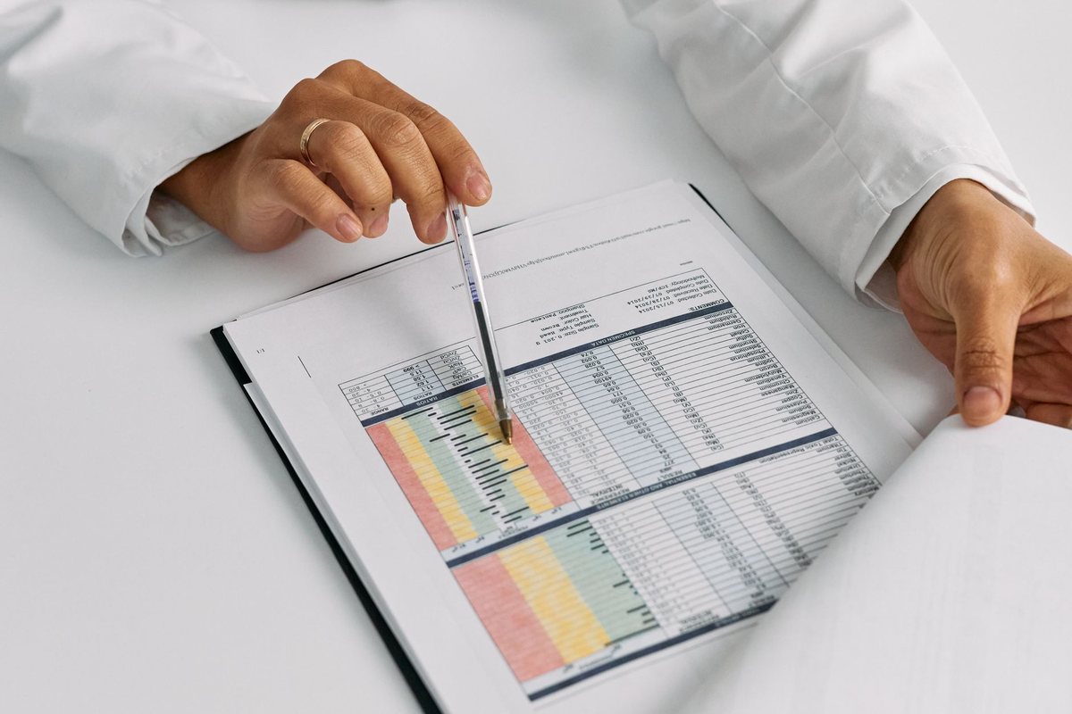 A reviewer in a lab coat working through tabulated clinical data with a pen