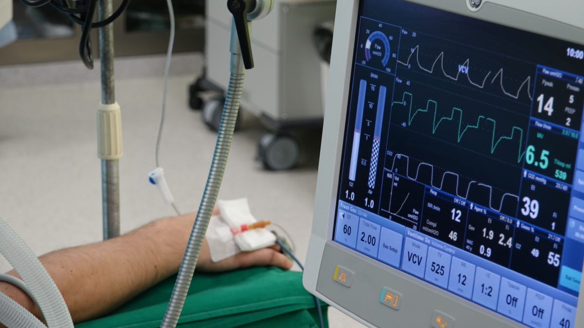 A close-up of a patient's hand connected to medical equipment in an ICU room