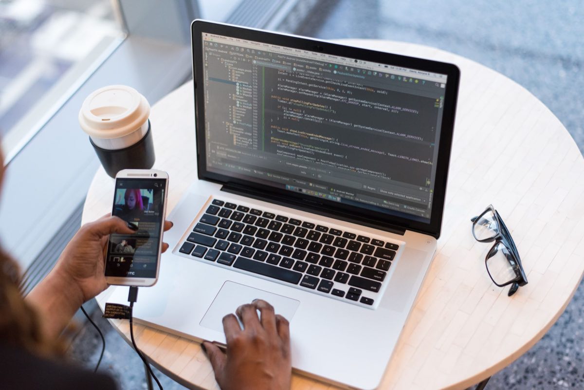 A programmer working across a laptop and smartphone at a cafe table