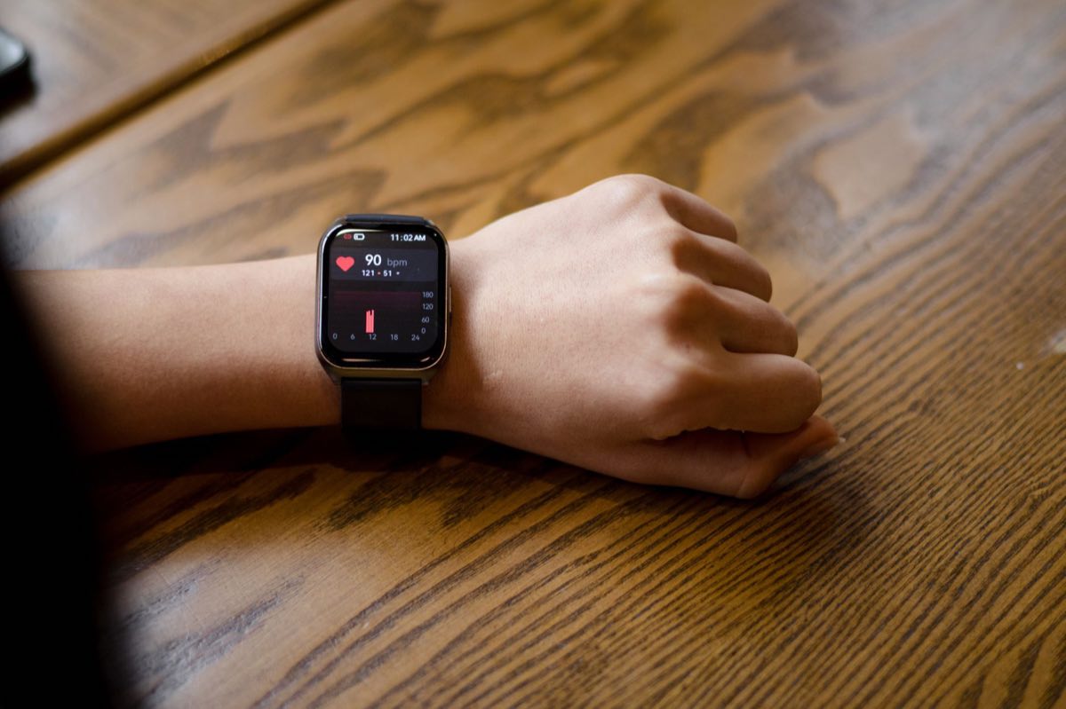 A smartwatch on a wrist displaying a heart rate of 90 bpm
