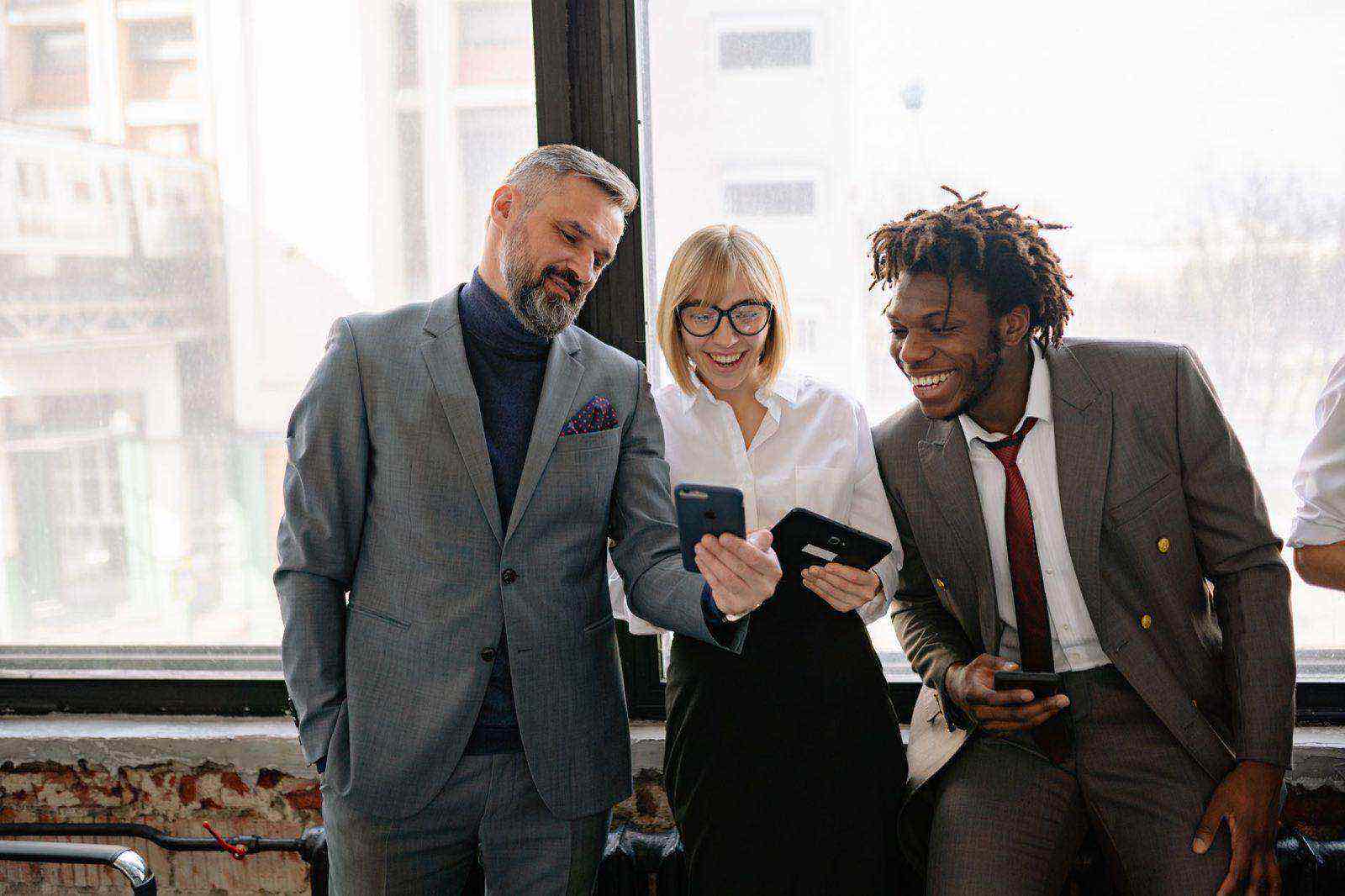 Three colleagues in a modern office comparing something on their phones