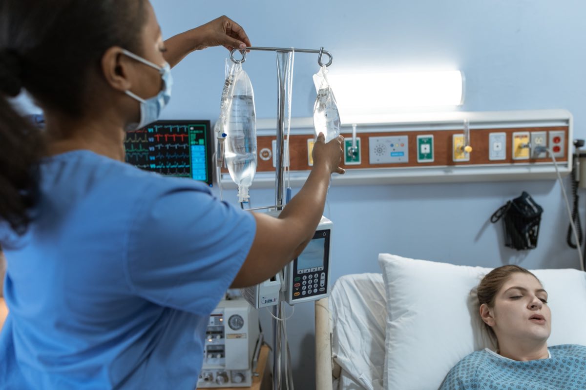 A nurse in a hospital setting adjusts an IV drip for a patient lying in bed, showcasing medical care
