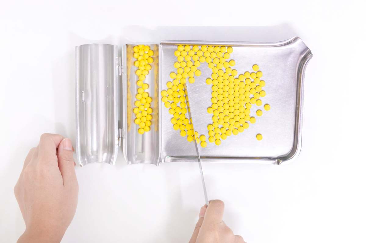 A pharmacy technician organizing tablets on a stainless steel tray