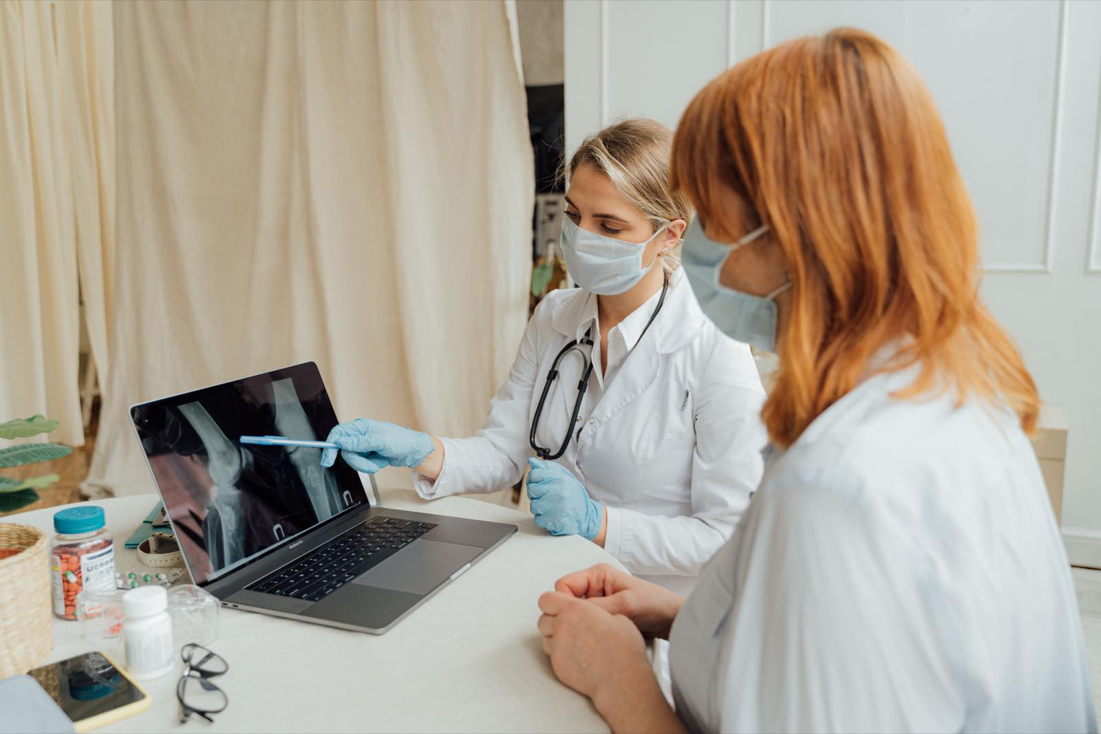 Doctor explains X-ray results to patient using a laptop in a clinic setting