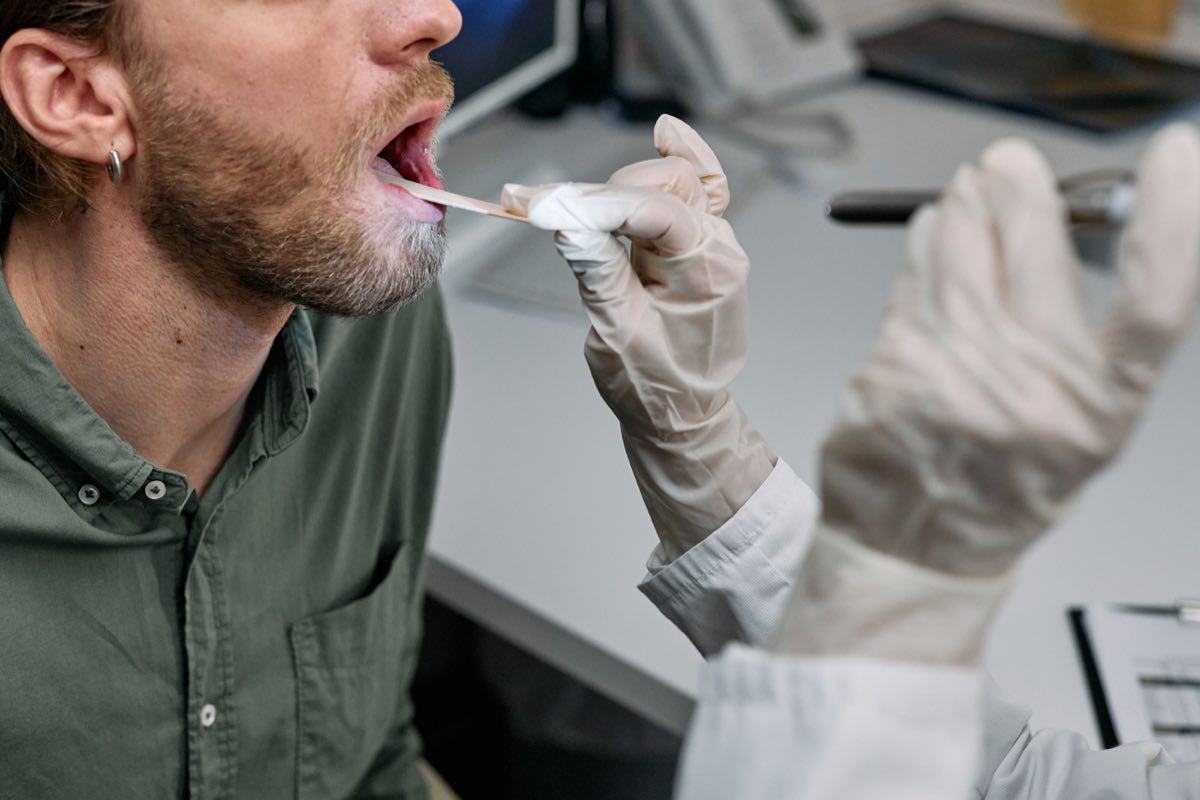 Close-up of a doctor examining a patient's throat with a tongue depressor in a clinical setting