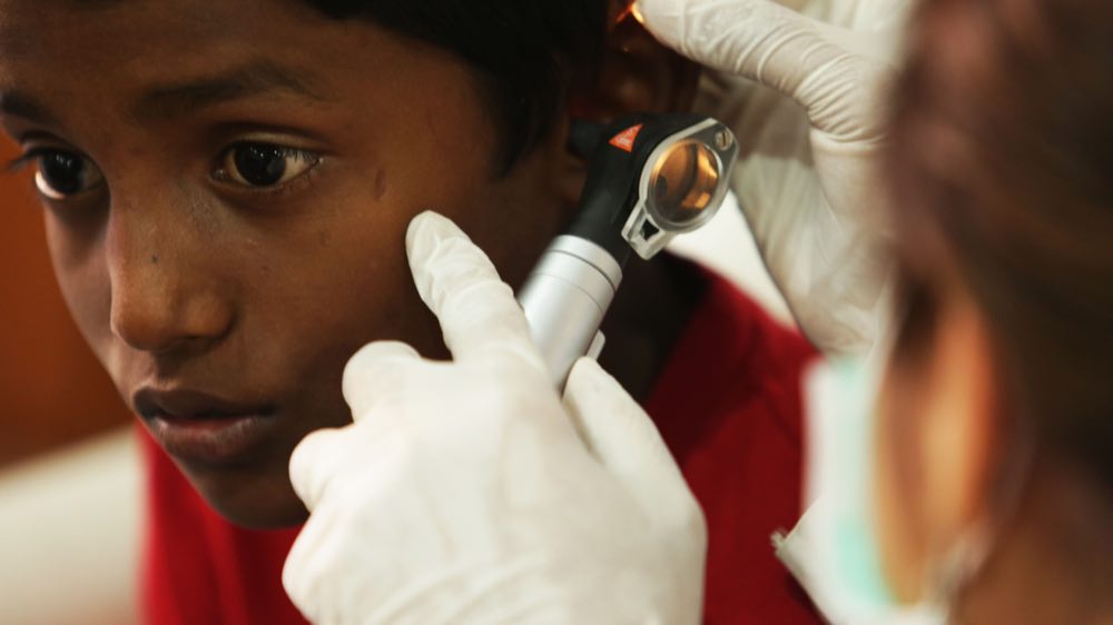 A young boy undergoes a routine ear examination by a medical professional using an otoscope