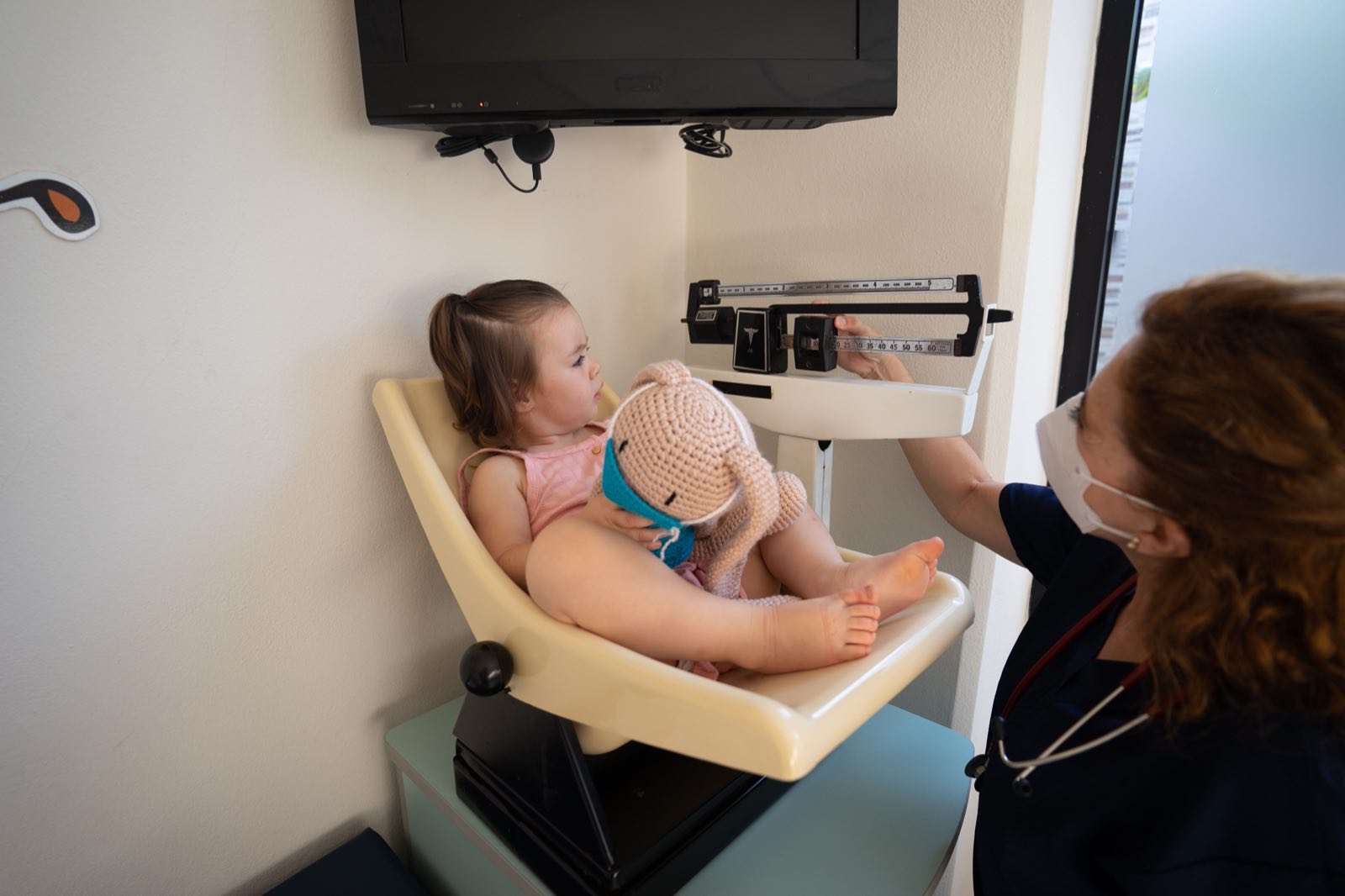 A young girl being weighed by a nurse in a pediatric examination room