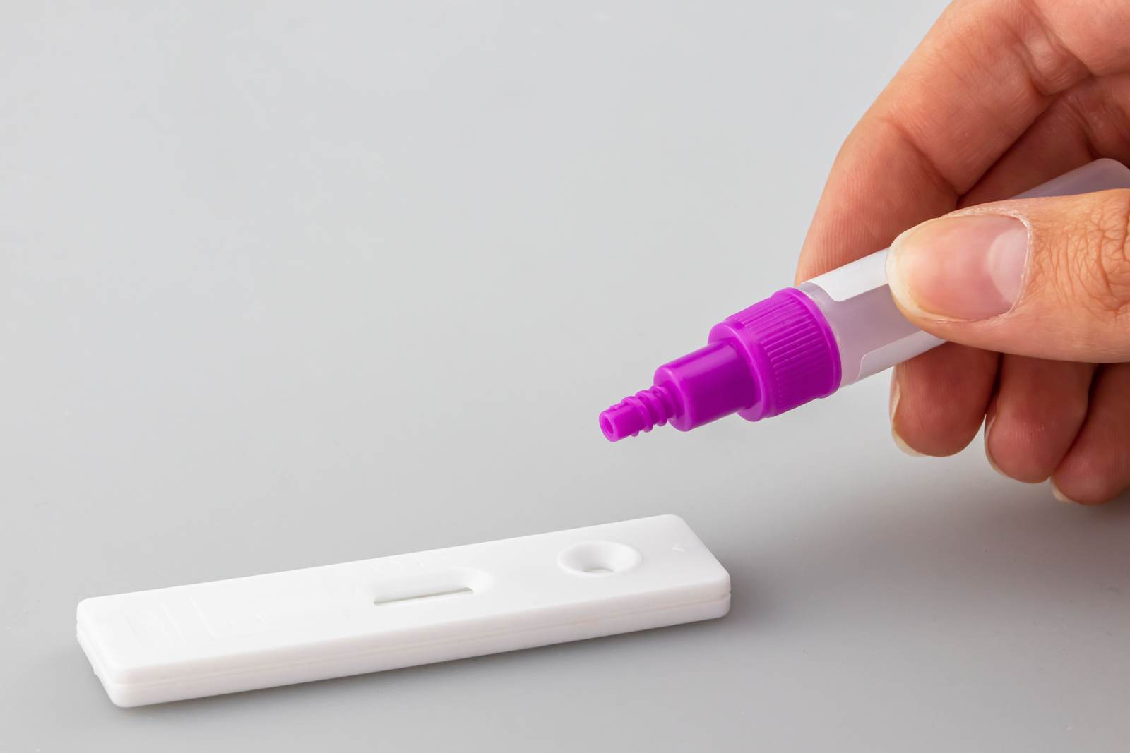 A hand applying liquid to a rapid diagnostic test kit