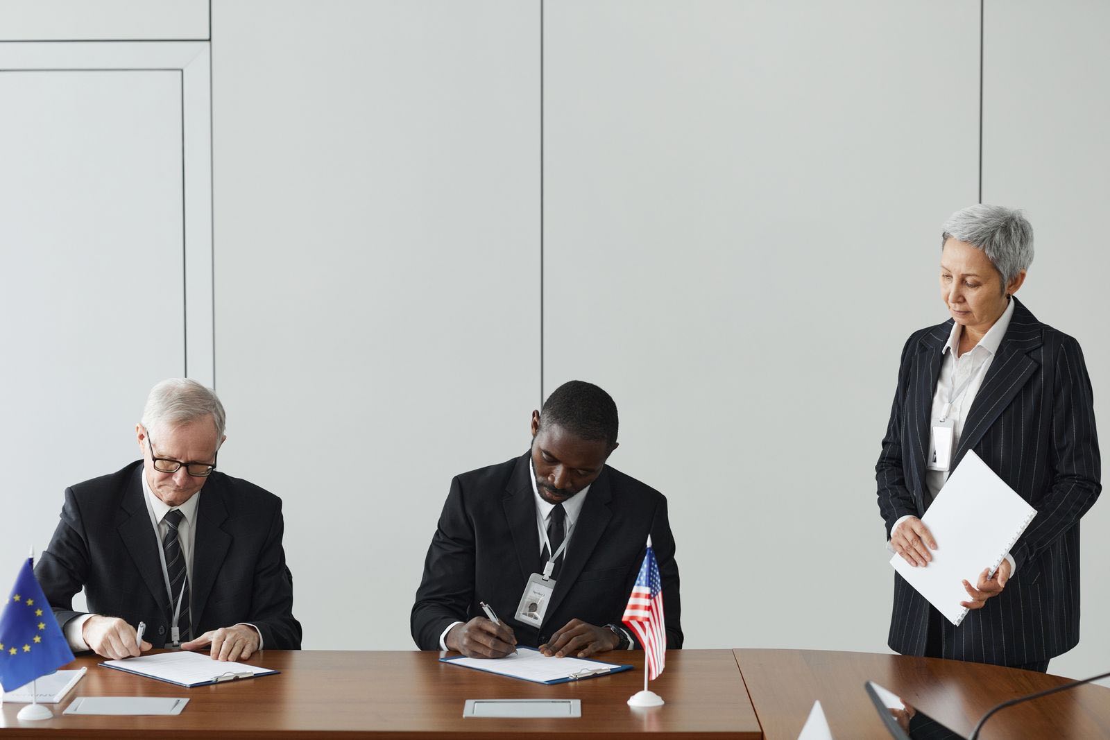 Regulatory delegates signing submission documents beside the flags of the European Union and the United States